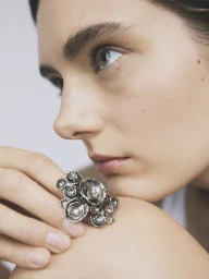 Close-up portrait of a woman resting her chin on her hand, showcasing a textured silver cluster ring.