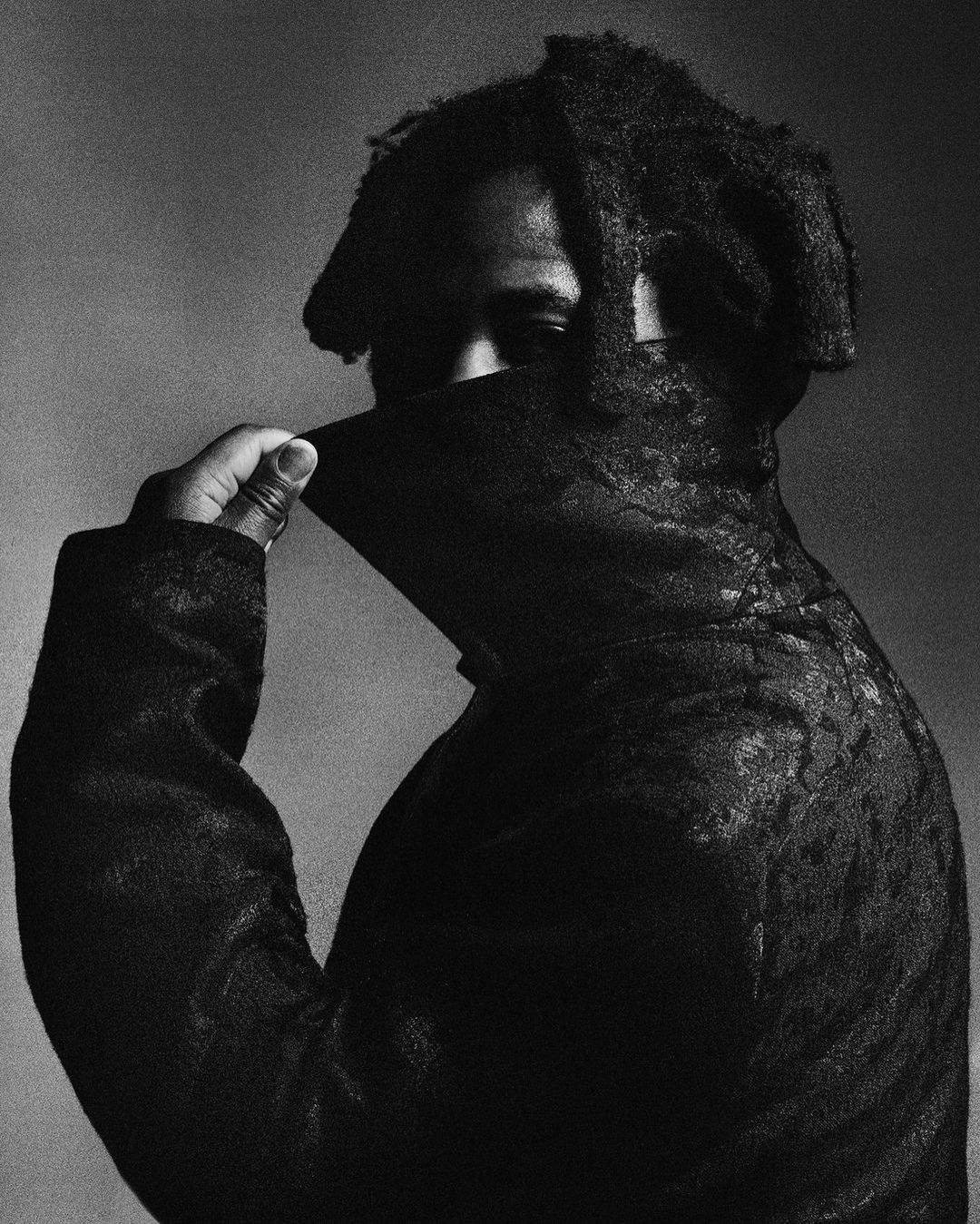 Portrait of Black man in high-contrast monochrome pulling coat collar up over his face
