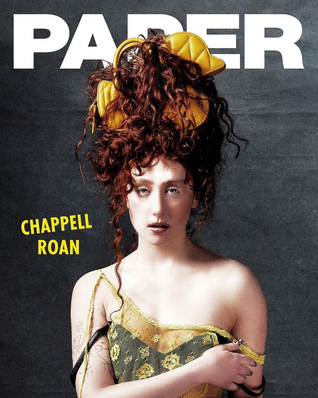 Magazine cover featuring Chappell Roan, portrait-style, red curly hair with yellow accessory, wearing green floral top, grey background.