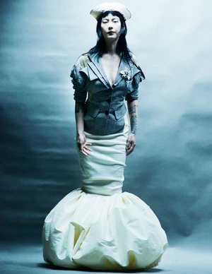Model wearing a grey tailored blazer and white voluminous gown against a grey gradient studio background.
