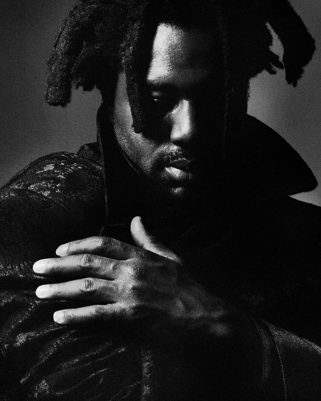 Portrait of Sampha with locs in a dark coat, hand resting on chest, photographed by Hector Clark for To Be Magazine