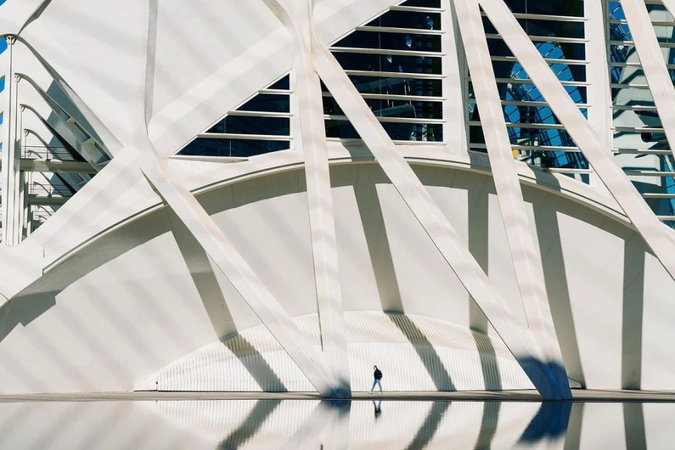 Person walking along the modern architecture of the City of Arts and Sciences in Valencia, Spain, with reflections in the water below.