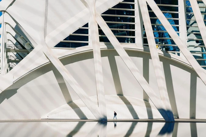 Person walking along the modern architecture of the City of Arts and Sciences in Valencia, Spain, with reflections in the water below.