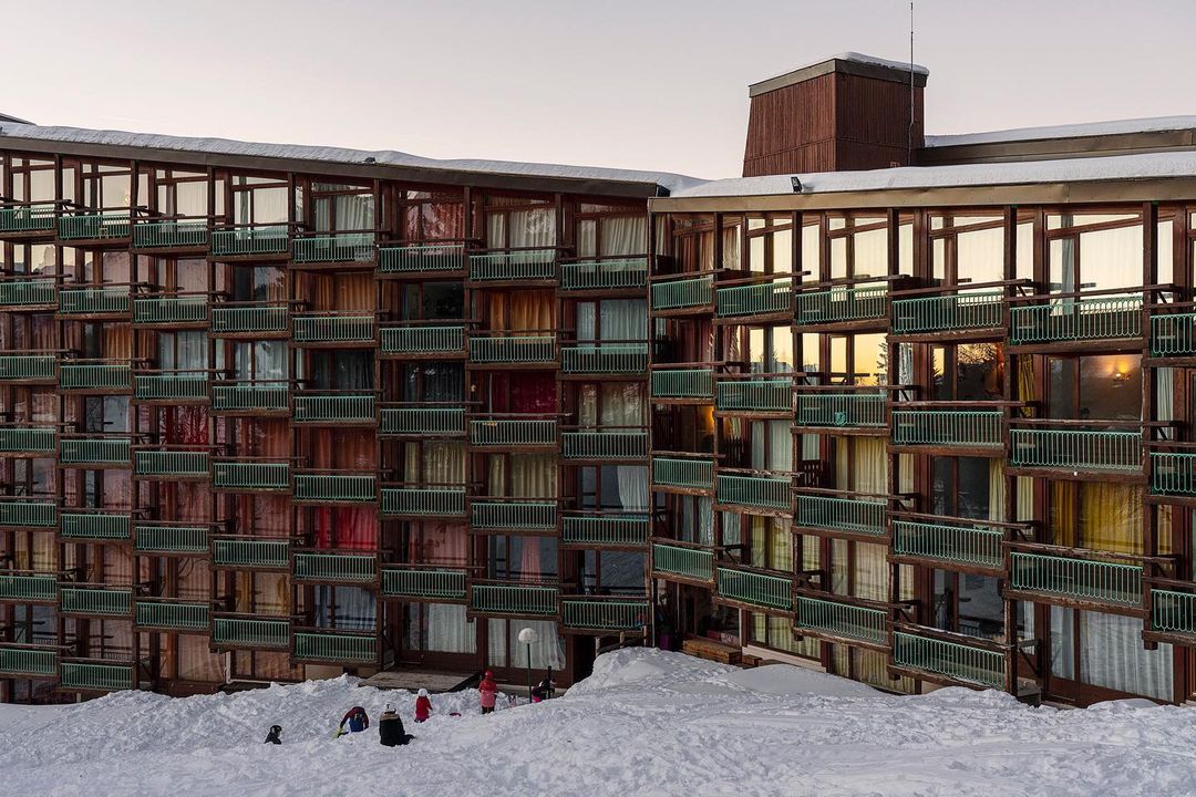 Exterior view of a ski resort apartment building with multiple balconies and snow-covered surroundings, children playing in the snow.