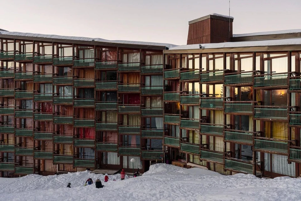 Exterior view of a ski resort apartment building with multiple balconies and snow-covered surroundings, children playing in the snow.