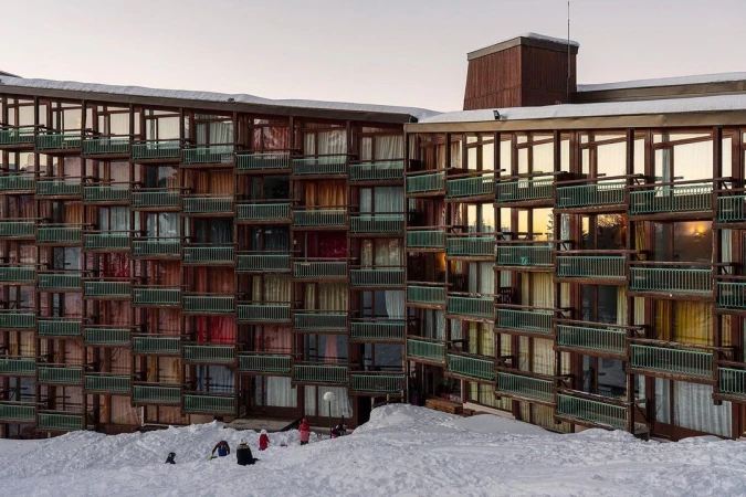 Exterior view of a ski resort apartment building with multiple balconies and snow-covered surroundings, children playing in the snow.
