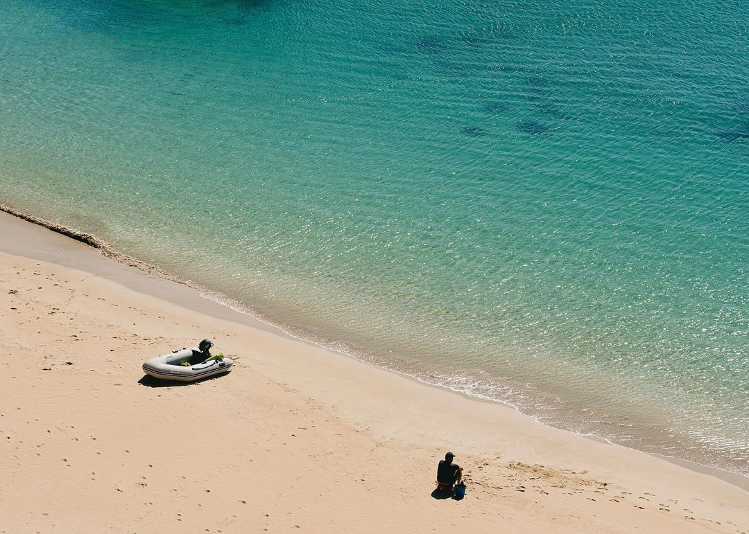 Overhead shot of tropical beach with turquoise water, an inflatable boat, and two people enjoying the scenic ocean view.