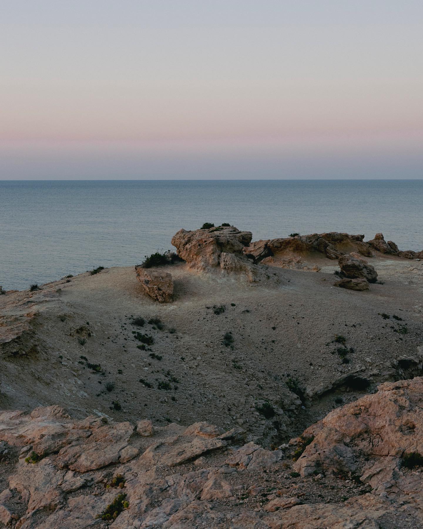 Ocean view with rocky cliffs under a pink and purple gradient sky at dusk, showcasing a serene coastal landscape.