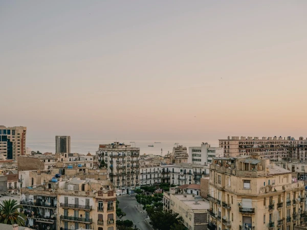 Cityscape view of buildings in Algiers, Algeria, featuring various architectural styles with the Mediterranean Sea in the background at daytime.