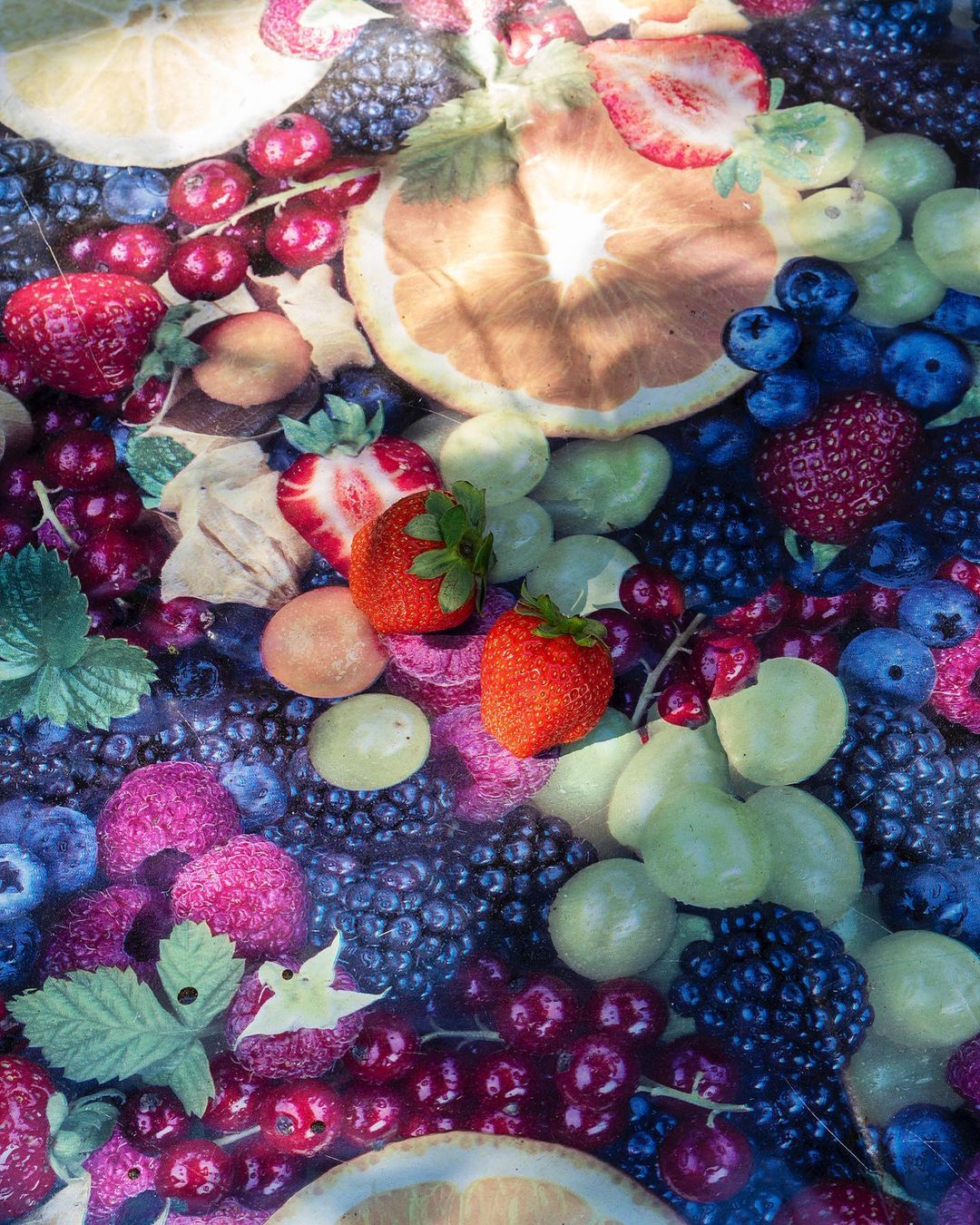 Overhead shot of vibrant mixed fruit including strawberries, blueberries, citrus slices, blackberries, and red currants filling the frame.