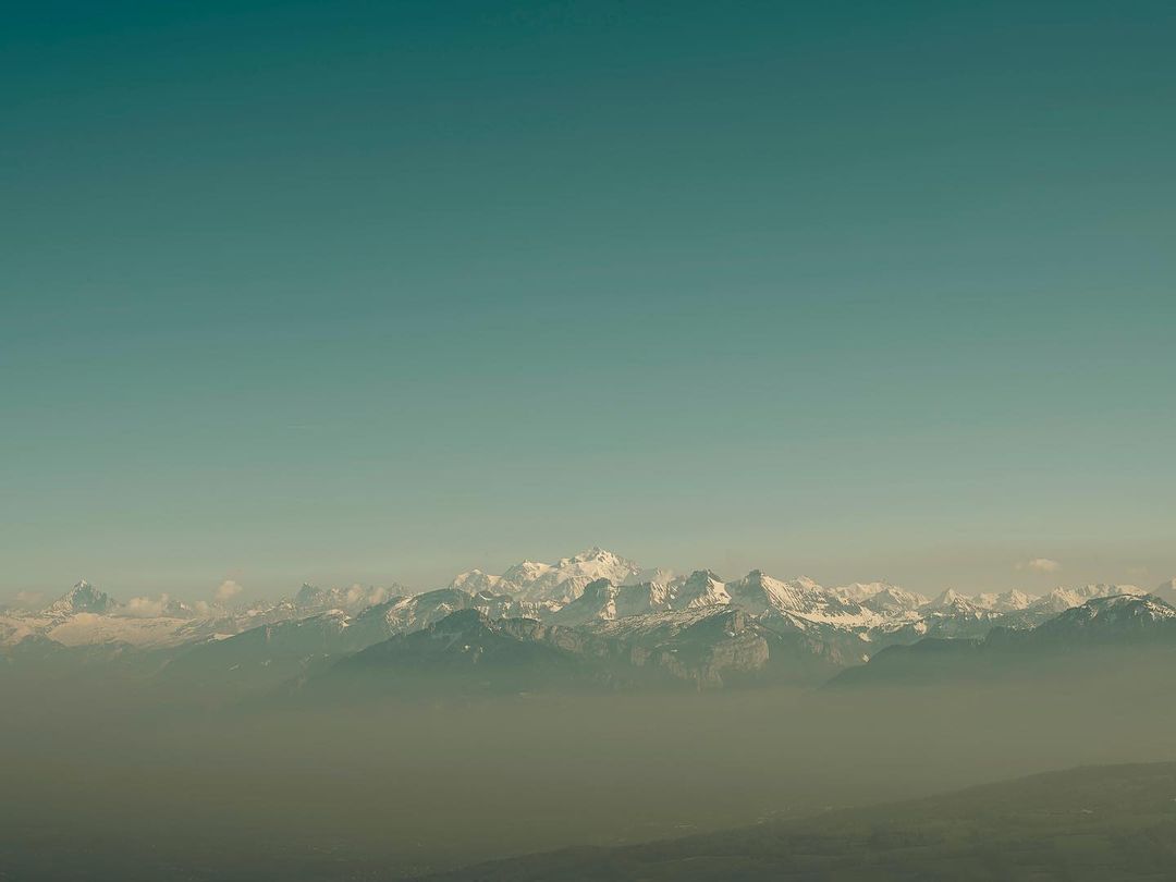 Scenic view of snow-capped mountains and a clear sky. Hazy conditions create a soft, muted color palette.
