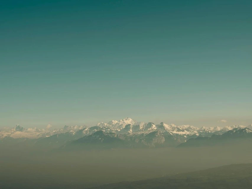 Scenic view of snow-capped mountains and a clear sky. Hazy conditions create a soft, muted color palette.