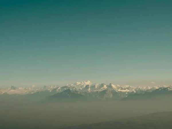 Scenic view of snow-capped mountains and a clear sky. Hazy conditions create a soft, muted color palette.
