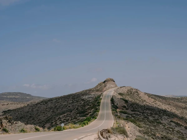 Scenic view of an asphalt road winding through a mountainous landscape under a clear blue sky, highlighting travel and nature.