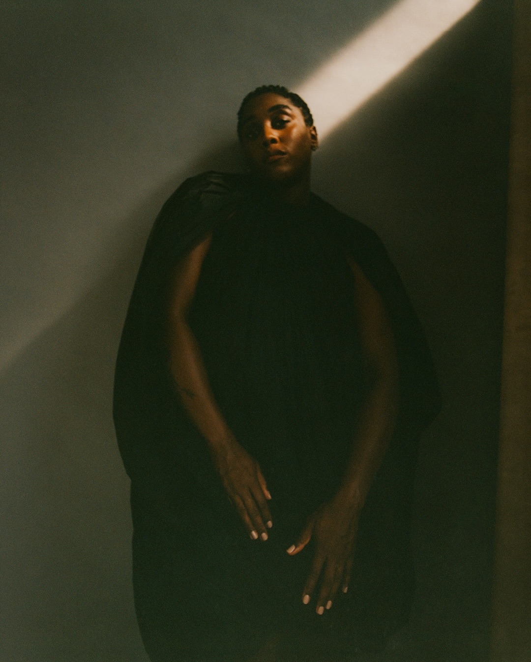 Dramatic portrait of a Black adult in dark clothing, captured in a photo studio with a single light source and a medium studio shot.
