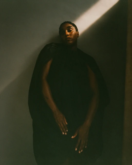 Dramatic portrait of a Black adult in dark clothing, captured in a photo studio with a single light source and a medium studio shot.