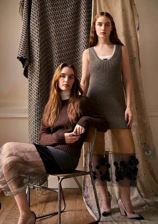 Two women pose indoors wearing knit dresses and skirts, one seated on a chair, neutral tones with a vintage and fashion editorial style.
