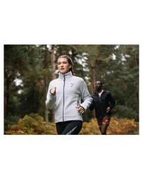 Woman in grey fleece jacket running along a forest path with a man running behind her