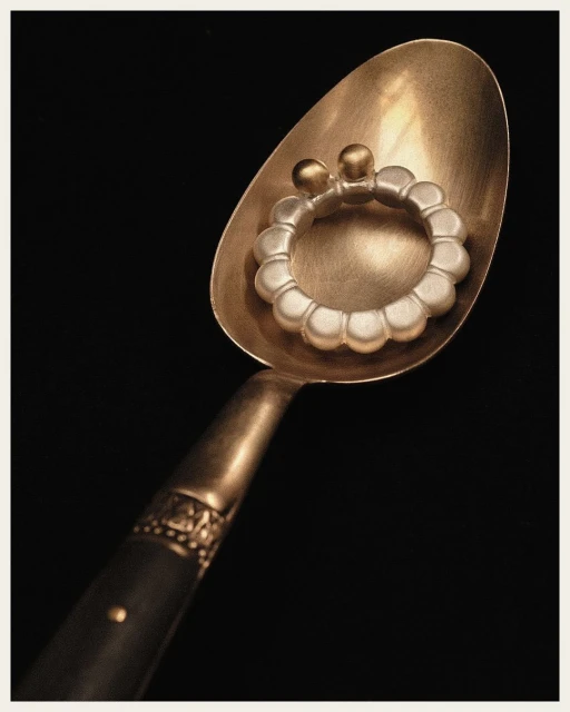 Close-up studio shot of a vintage silver spoon holding a modern silver baby bracelet against a solid black background.