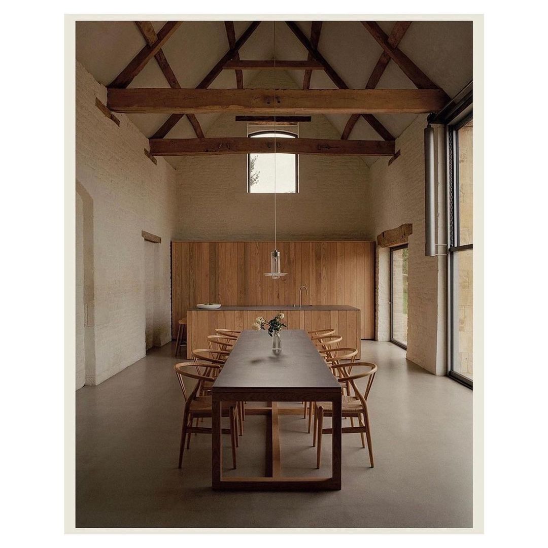 Interior of a dining room with a long wooden table and matching chairs, set in a renovated barn with a high-vaulted ceiling.