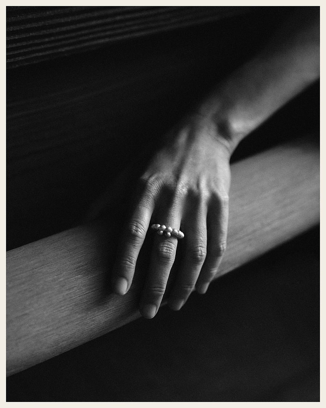 Close-up shot of a fair-skinned hand resting on a ledge, adorned with a pearl ring on the middle finger in a muted color palette.