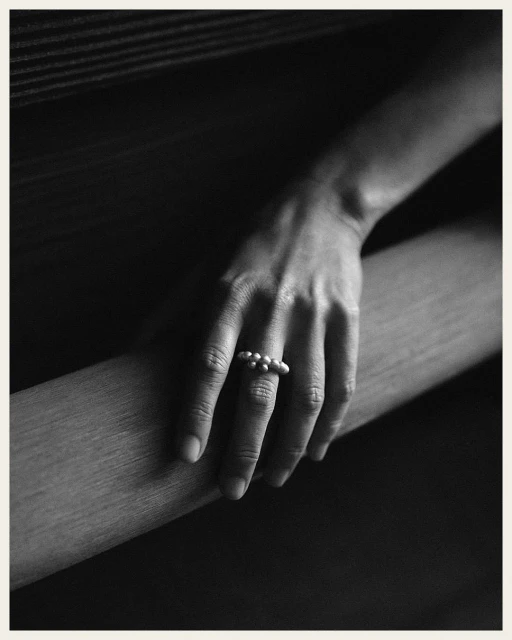 Close-up shot of a fair-skinned hand resting on a ledge, adorned with a pearl ring on the middle finger in a muted color palette.
