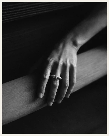 Close-up shot of a fair-skinned hand resting on a ledge, adorned with a pearl ring on the middle finger in a muted color palette.