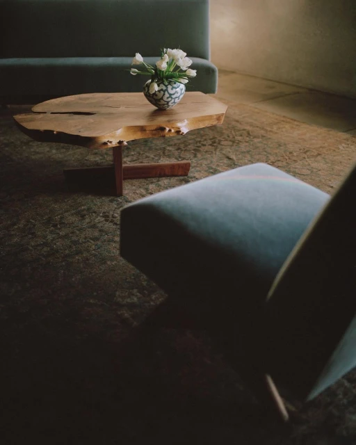 Interior design with light blue upholstered furniture, a wooden coffee table with a vase of white tulips, and a textured floor.