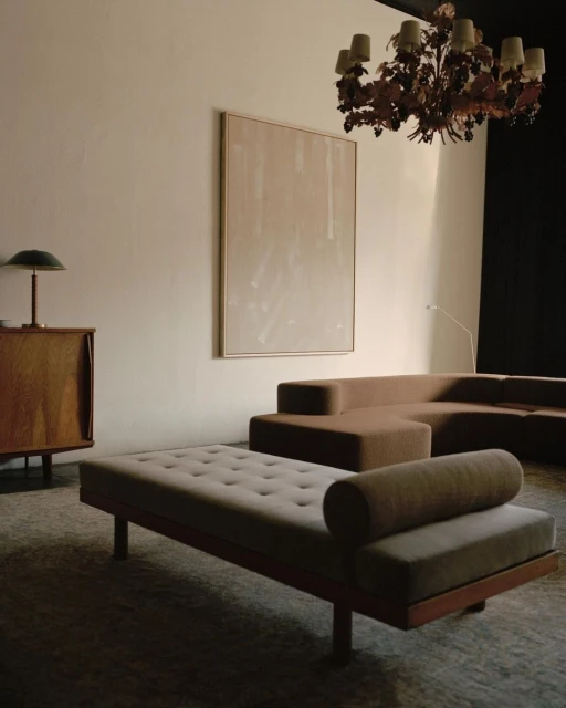 Living room interior featuring neutral tones, a modern sofa, chaise lounge, abstract wall art, a vintage-style chandelier, and wood cabinet.