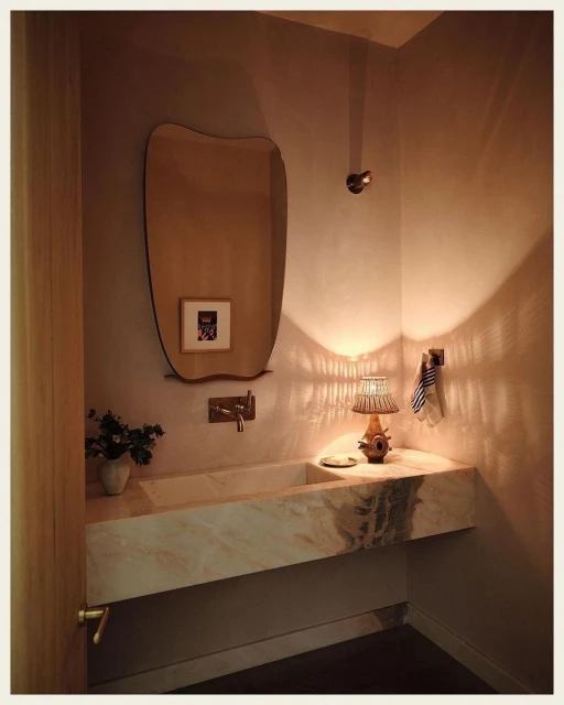 Contemporary bathroom interior featuring a marble vanity, uniquely shaped mirror, warm lighting, and neutral color palette for a modern design.