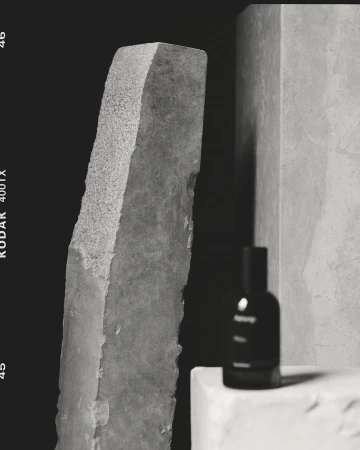 Black and white product photography of a glass perfume bottle on a plinth with rough stone monoliths by Rich Stapleton.