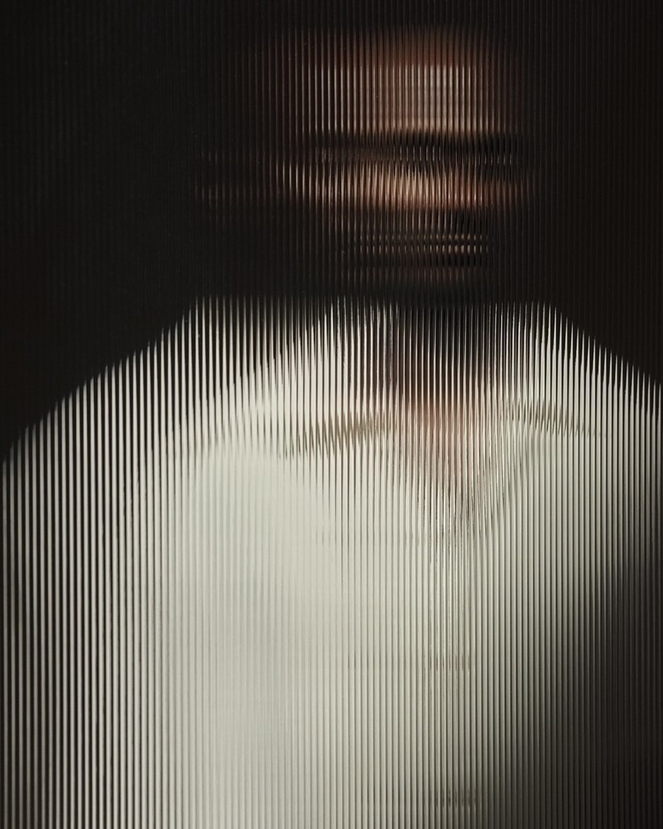 Abstract portrait of a person behind a textured glass or plastic screen, with light filtering through and creating an obscured view.