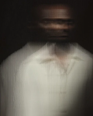 Abstract portrait of a person behind a textured glass or plastic screen, with light filtering through and creating an obscured view.