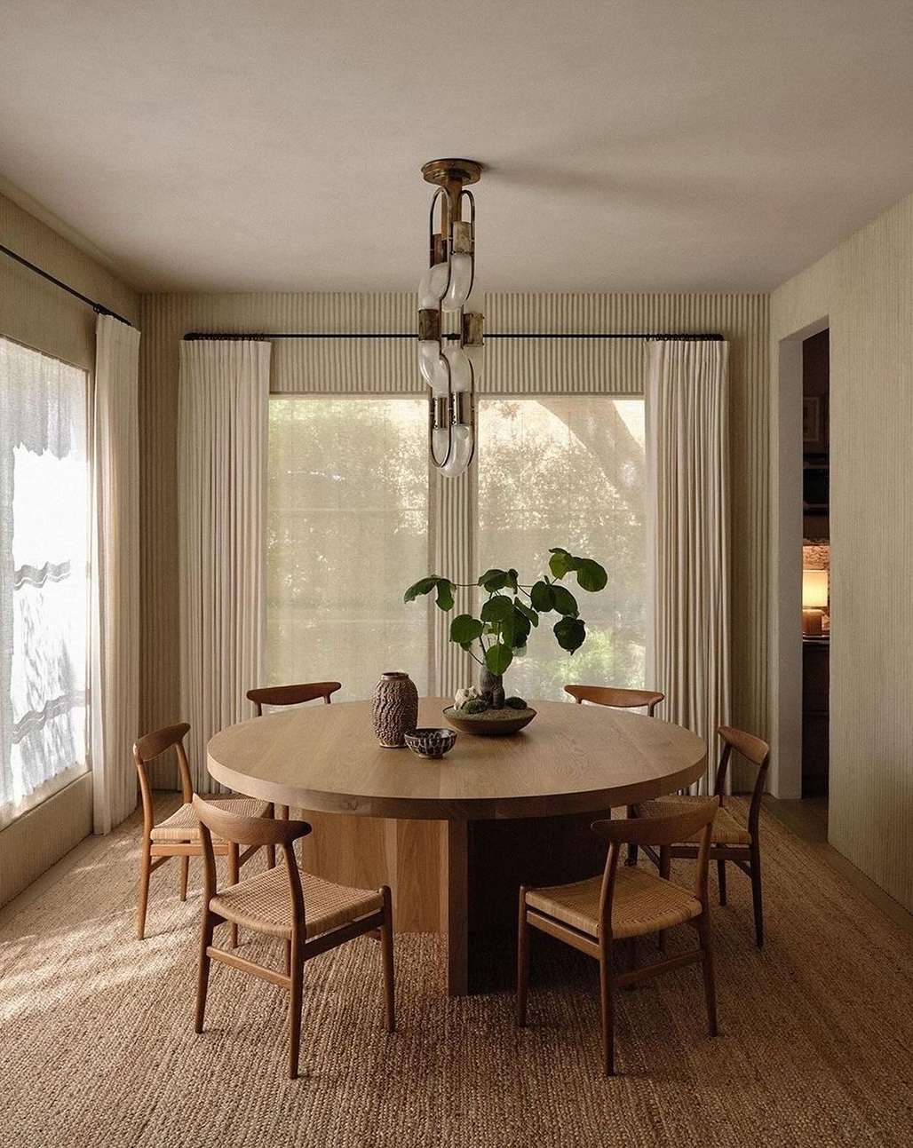 Indoor dining room featuring a round wooden table with six chairs, a woven rug, and a unique light fixture, creating a warm and inviting space.