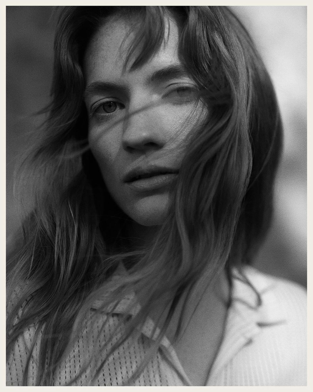 Close-up monochrome portrait of a woman with long hair blowing across her face wearing a textured shirt by Rich Stapleton