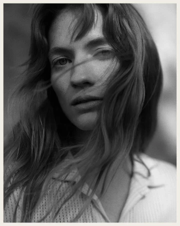 Close-up monochrome portrait of a woman with long hair blowing across her face wearing a textured shirt by Rich Stapleton