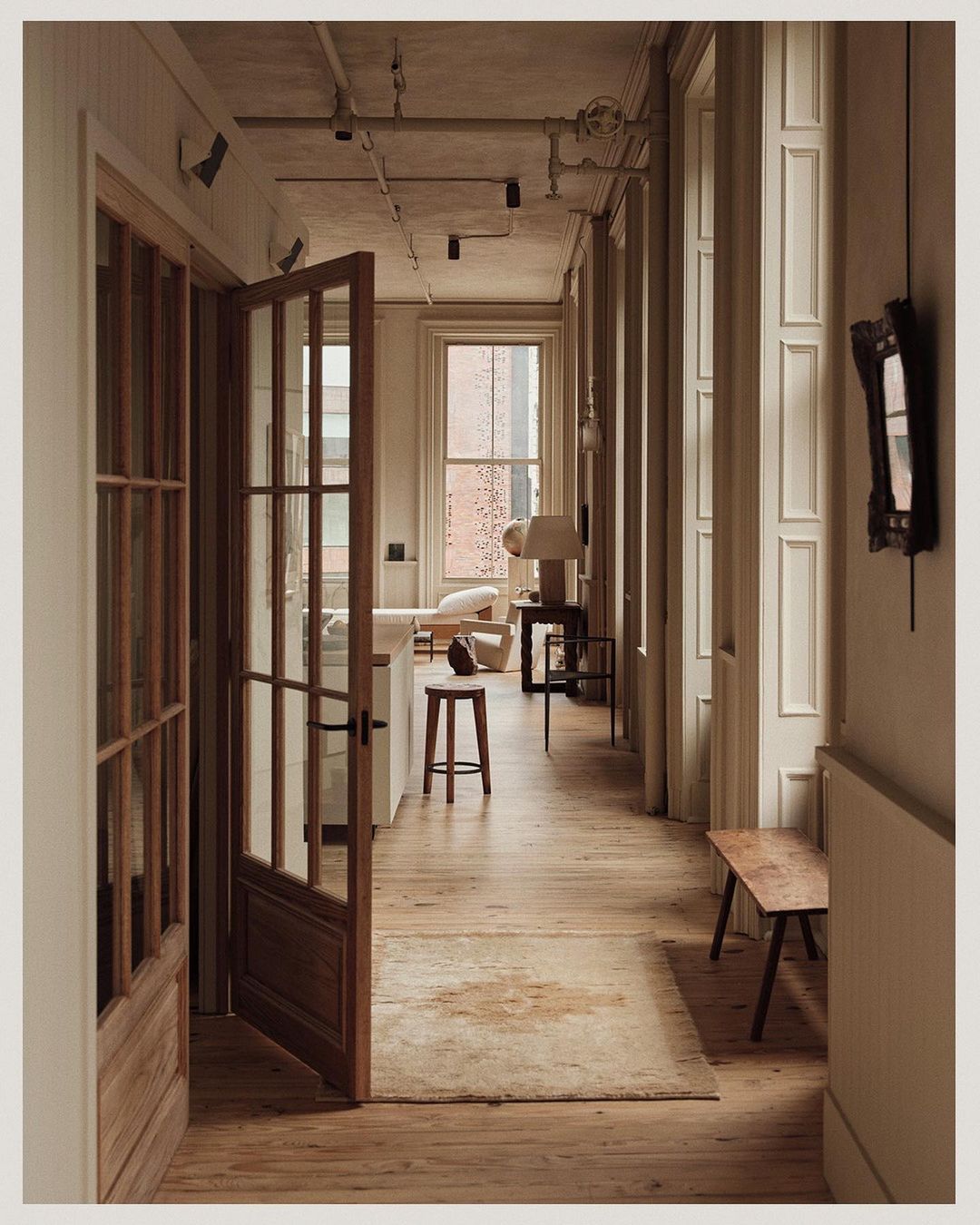 Hallway interior with wood floors, rug, open doorway, and natural light from windows, creating a warm, inviting atmosphere.