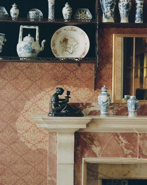 Interior design with antique porcelain on a shelf and fireplace mantel, featuring decorative wallpaper and marble fireplace surround.