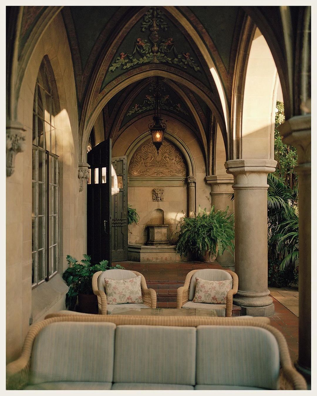 Exterior architectural shot of an outdoor courtyard with arched walkways, neutral furniture, stone pillars, and decorative details.