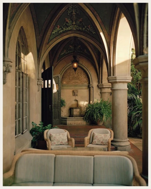 Exterior architectural shot of an outdoor courtyard with arched walkways, neutral furniture, stone pillars, and decorative details.