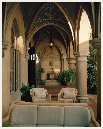 Exterior architectural shot of an outdoor courtyard with arched walkways, neutral furniture, stone pillars, and decorative details.