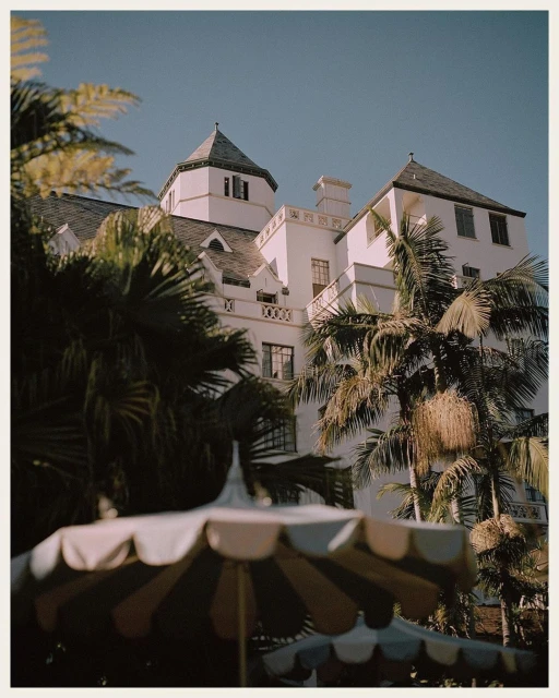 Exterior daytime shot of a large white building with turrets, surrounded by palm trees, and visible umbrellas in the foreground.