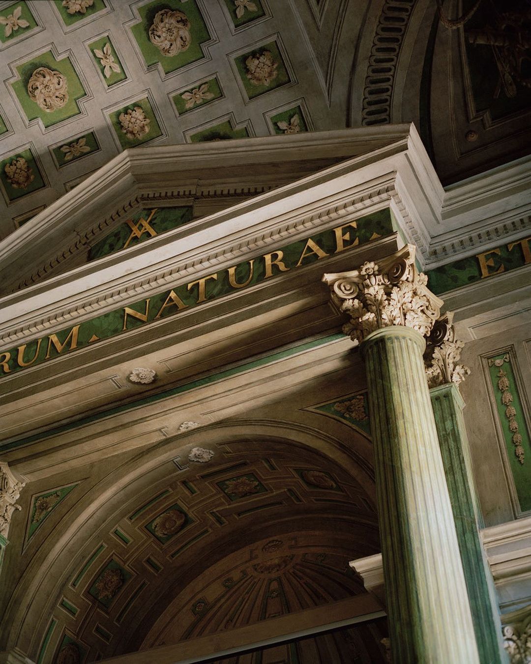 Architectural detail of a classical building interior featuring a column, archway, and ornate ceiling decorations in green and white tones.