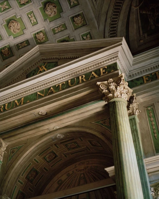 Architectural detail of a classical building interior featuring a column, archway, and ornate ceiling decorations in green and white tones.