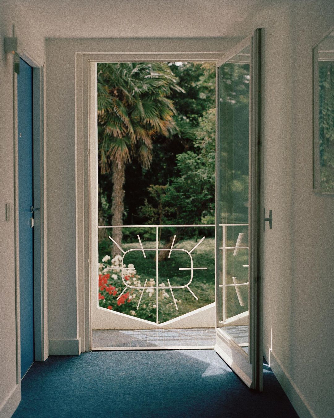 View through open door onto a sunny patio with flowers and tropical trees, showcasing an inviting indoor-outdoor transition.
