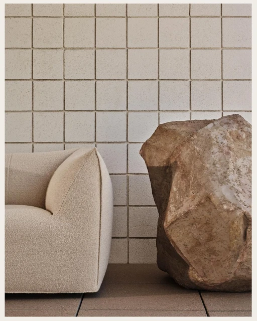 Interior featuring a cream-colored couch alongside a large, irregularly shaped rock sculpture, set against a backdrop of tiled walls.