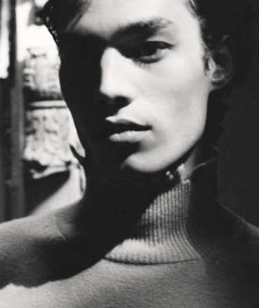 Close-up monochrome portrait of a young man wearing a high-neck sweater with dramatic high-contrast lighting.