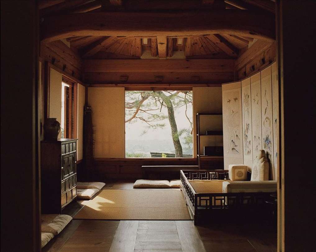Tranquil interior featuring a traditional Korean bed, wooden furniture, and serene view through a window, showcasing peaceful home decor.