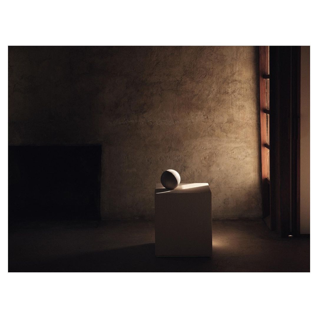 Abstract composition in room featuring a sphere on a cubic pedestal, illuminated by a focused spotlight, against textured wall.