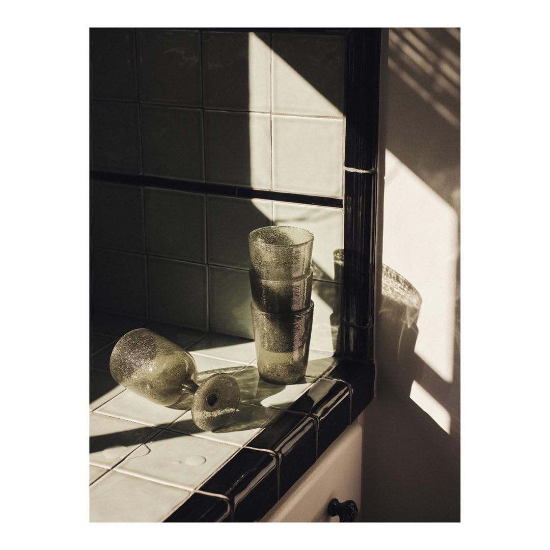 Still life composition of three glasses stacked, one glass lying on its side, and a rounded object, all on a tiled surface in natural light.